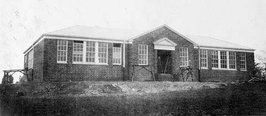 Black and white photograph of the original front entrance of Franconia Elementary School during construction in 1931. Workbenches and materials are visible in front of the building. The walls, windows, and roof are all in place. 